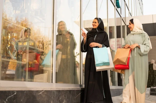 الشراء في أيام التنزيلات والتخفيضات، الاستمتاع بالشراء من المول، متعة التسوق في الجمعه البيضاء مع الاصدقاء، سيدتان عربيتان خليجيتان سعوديتان ترتديان العباءه والحجاب تحملان حقائب التسوق بتعابير وايماءات السعادة والسرور