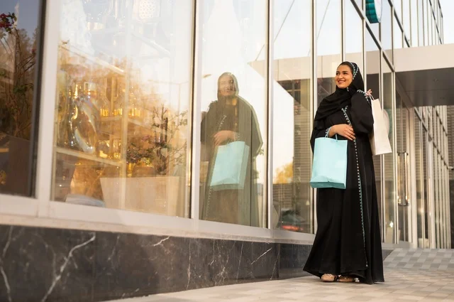 Exploiting seasonal offers and discounts, as well as Black Friday, shopping from commercial centers, choosing supplies from the shopping mall, an Arab Gulf Saudi woman wearing an abaya and hijab carrying paper bags in her hand.