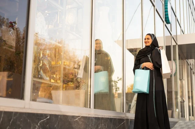 Exploiting seasonal offers and discounts, as well as Black Friday, shopping from commercial centers, choosing supplies from the shopping mall, an Arab Gulf Saudi woman wearing an abaya and hijab carrying paper bags in her hand.