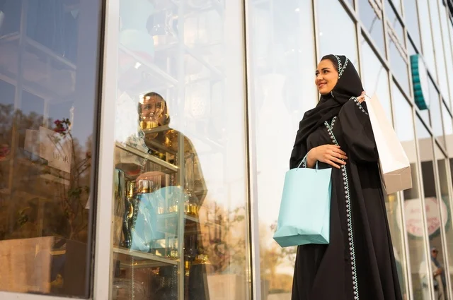 Exploiting seasonal offers and discounts, as well as Black Friday, shopping from commercial centers, choosing supplies from the shopping mall, an Arab Gulf Saudi woman wearing an abaya and hijab carrying paper bags in her hand.
