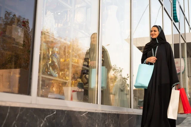 Exploiting seasonal offers and discounts, as well as Black Friday, shopping from commercial centers, choosing supplies from the shopping mall, an Arab Gulf Saudi woman wearing an abaya and hijab carrying paper bags in her hand.