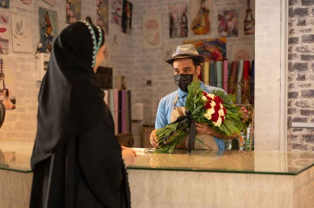 متاجر ومحلات بيع الورود والزهور الطبيعية للأعياد والمناسبات, امرأة عربية خليجية سعودية ترتدي العباءة والحجاب تقوم بشراء باقة ورد احمر طبيعي من البائع , ايماءات تدل على الفرح والسعاده