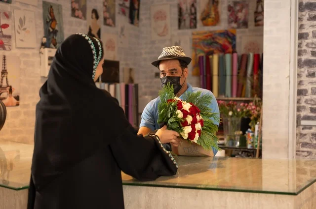 Shops and stores selling flowers and natural flowers for holidays and occasions, a Saudi Arabian Gulf woman wearing an abaya and hijab buying a bouquet of natural red roses from the seller, gestures indicating joy and happiness