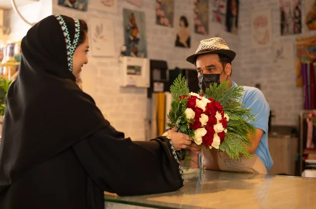 متاجر ومحلات بيع الورود والزهور الطبيعية للأعياد والمناسبات, امرأة عربية خليجية سعودية ترتدي العباءة والحجاب تقوم بشراء باقة ورد احمر طبيعي من البائع , ايماءات تدل على الفرح والسعاده