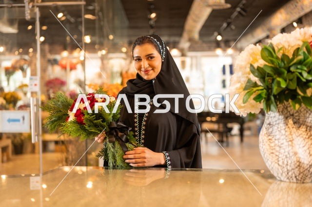 محلات ومتاجر بيع وشراء الورود والزهور الطبيعية للأعياد والمناسبات, امرأة عربية خليجية سعودية ترتدي العباءة والحجاب تحمل باقة ورد احمر طبيعي تنظر الى الكاميرا بايماءات تدل على الفرح والسعاده