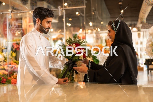 تعابير وايماءات المودة والسعاده، محلات ومتاجر بيع وشراء الورود والزهور الطبيعية للأعياد والمناسبات, زوج عربي خليجي سعودي يرتدي الثوب التقليدي يقوم بإهداء باقة ورد احمر طبيعي لزوجته