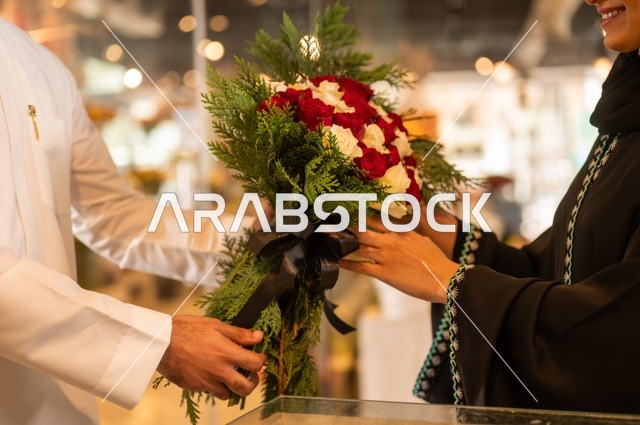 تعابير وايماءات المودة والسعاده، محلات ومتاجر بيع وشراء الورود والزهور الطبيعية للأعياد والمناسبات, زوج عربي خليجي سعودي يرتدي الثوب التقليدي يقوم بإهداء باقة ورد احمر طبيعي لزوجته