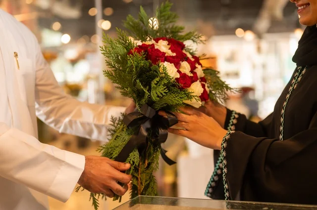 تعابير وايماءات المودة والسعاده، محلات ومتاجر بيع وشراء الورود والزهور الطبيعية للأعياد والمناسبات, زوج عربي خليجي سعودي يرتدي الثوب التقليدي يقوم بإهداء باقة ورد احمر طبيعي لزوجته