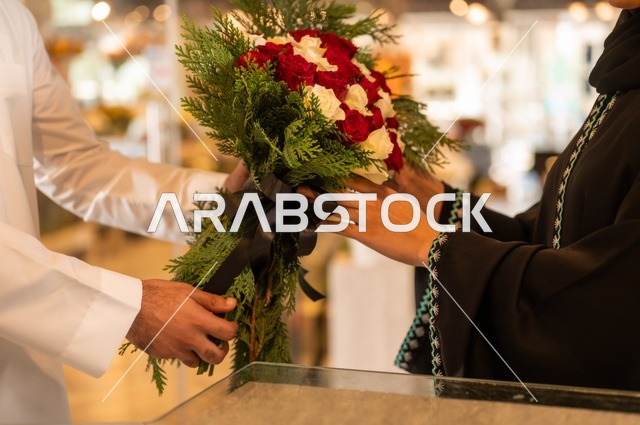 تعابير وايماءات المودة والسعاده، محلات ومتاجر بيع وشراء الورود والزهور الطبيعية للأعياد والمناسبات, زوج عربي خليجي سعودي يرتدي الثوب التقليدي يقوم بإهداء باقة ورد احمر طبيعي لزوجته