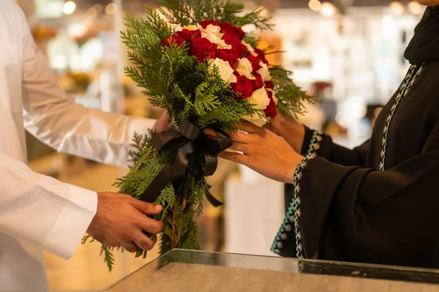 تعابير وايماءات المودة والسعاده، محلات ومتاجر بيع وشراء الورود والزهور الطبيعية للأعياد والمناسبات, زوج عربي خليجي سعودي يرتدي الثوب التقليدي يقوم بإهداء باقة ورد احمر طبيعي لزوجته