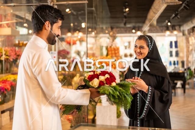 تعابير وايماءات المودة والسعاده، محلات ومتاجر بيع وشراء الورود والزهور الطبيعية للأعياد والمناسبات, زوج عربي خليجي سعودي يرتدي الثوب التقليدي يقوم بإهداء باقة ورد احمر طبيعي لزوجته