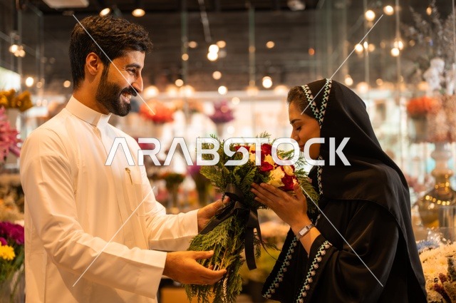 تعابير وايماءات المودة والسعاده، محلات ومتاجر بيع وشراء الورود والزهور الطبيعية للأعياد والمناسبات, زوج عربي خليجي سعودي يرتدي الثوب التقليدي يقوم بإهداء باقة ورد احمر طبيعي لزوجته
