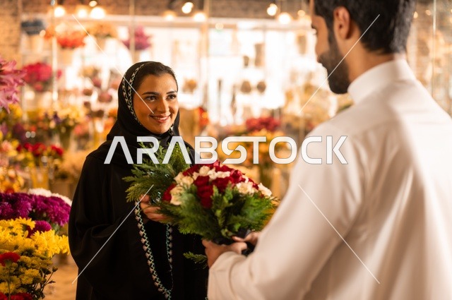 تعابير وايماءات المودة والسعاده، محلات ومتاجر بيع وشراء الورود والزهور الطبيعية للأعياد والمناسبات, زوج عربي خليجي سعودي يرتدي الثوب التقليدي يقوم بإهداء باقة ورد احمر طبيعي لزوجته