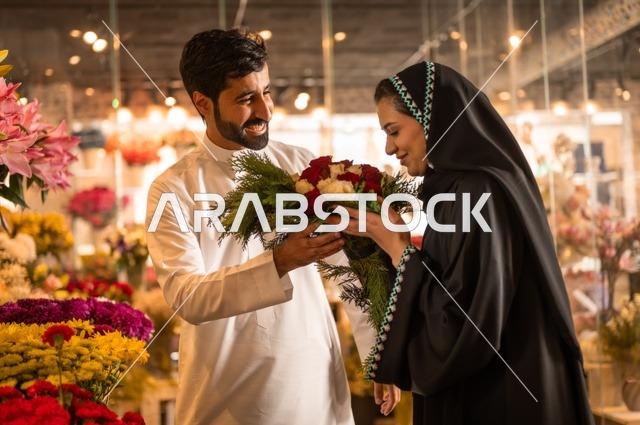 تعابير وايماءات المودة والسعاده، محلات ومتاجر بيع وشراء الورود والزهور الطبيعية للأعياد والمناسبات, زوج عربي خليجي سعودي يرتدي الثوب التقليدي يقوم بإهداء باقة ورد احمر طبيعي لزوجته
