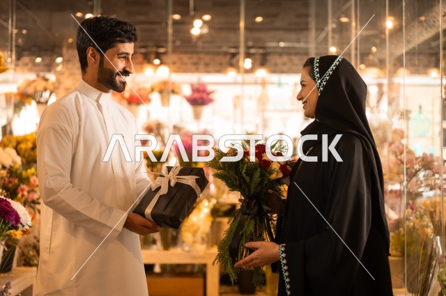 زوج عربي خليجي سعودي يرتدي الثوب التقليدي يقوم بإهداء باقة ورد احمر طبيعي وهدية مغلفة لزوجته، تعابير وايماءات المودة والسعاده، محلات ومتاجر بيع وشراء الورود والزهور الطبيعية للأعياد والمناسبات