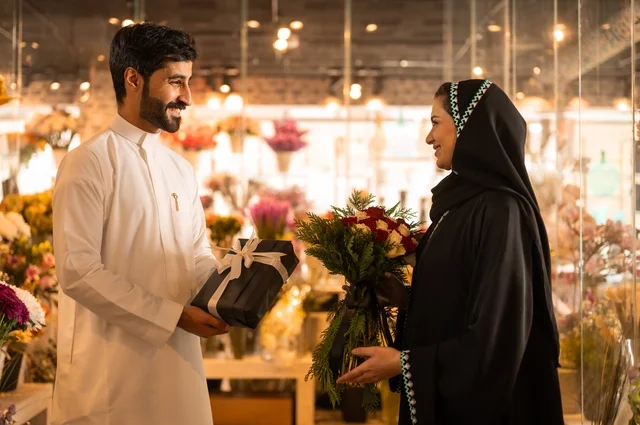زوج عربي خليجي سعودي يرتدي الثوب التقليدي يقوم بإهداء باقة ورد احمر طبيعي وهدية مغلفة لزوجته، تعابير وايماءات المودة والسعاده، محلات ومتاجر بيع وشراء الورود والزهور الطبيعية للأعياد والمناسبات