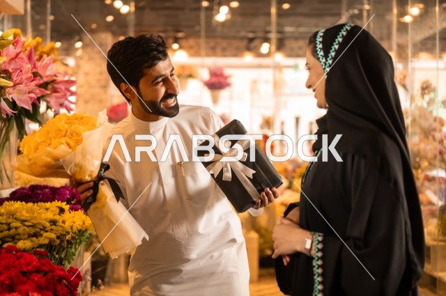 زوج عربي خليجي سعودي يرتدي الثوب التقليدي يقوم بإهداء باقة ورد احمر طبيعي وهدية مغلفة لزوجته، تعابير وايماءات المودة والسعاده، محلات ومتاجر بيع وشراء الورود والزهور الطبيعية للأعياد والمناسبات