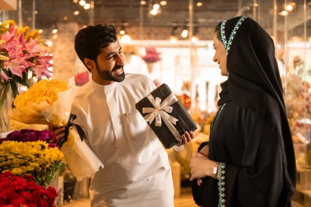 زوج عربي خليجي سعودي يرتدي الثوب التقليدي يقوم بإهداء باقة ورد احمر طبيعي وهدية مغلفة لزوجته، تعابير وايماءات المودة والسعاده، محلات ومتاجر بيع وشراء الورود والزهور الطبيعية للأعياد والمناسبات