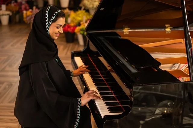 Music and entertainment activities, presenting programs and musical arts and theatrical art, a Gulf Saudi Arabian woman artist sitting in front of a musical piano enjoying playing, musical artistic talents, spending time playing string instruments.