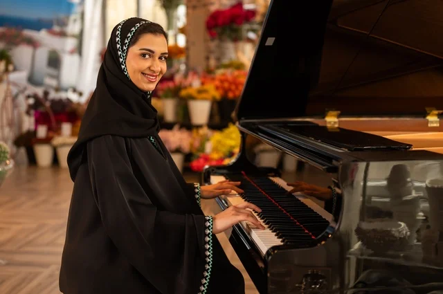 الطرب والانشطة ترفيهية، تقديم البرامج والفنون الموسيقية والفن المسرحي، إمراة خليجية سعودية عربية فنانة تجلس امام آلة البيانو الموسيقية تستمتع بالعزف، مواهب فنية موسيقية، قضاء الوقت بالعزف على الألات الوترية