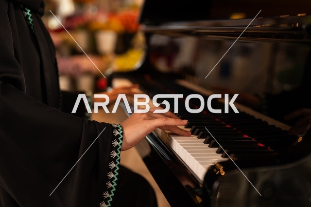 الطرب والانشطة ترفيهية، تقديم البرامج والفنون الموسيقية والفن المسرحي، إمراة خليجية سعودية عربية فنانة تجلس امام آلة البيانو الموسيقية تستمتع بالعزف، مواهب فنية موسيقية، قضاء الوقت بالعزف على الألات الوترية