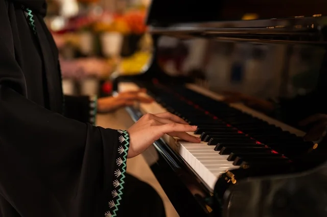 الطرب والانشطة ترفيهية، تقديم البرامج والفنون الموسيقية والفن المسرحي، إمراة خليجية سعودية عربية فنانة تجلس امام آلة البيانو الموسيقية تستمتع بالعزف، مواهب فنية موسيقية، قضاء الوقت بالعزف على الألات الوترية