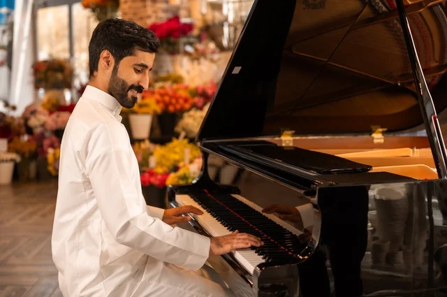 مواهب فنية موسيقية، قضاء الوقت بالعزف على الألات الوترية، الطرب والانشطة ترفيهية، تقديم البرامج والفنون الموسيقية والفن المسرحي، رجل خليجي سعودي عربي فنان يجلس امام آلة البيانو الموسيقية ويستمتع بالعزف