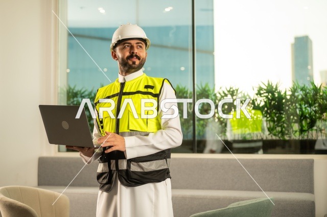 Reviewing new architectural designs on a laptop, an Arab Saudi Gulf architect wearing work attire uses a laptop, electronic supervision of the implementation of architectural engineering projects and plans in construction, integrating work with technology and technology.