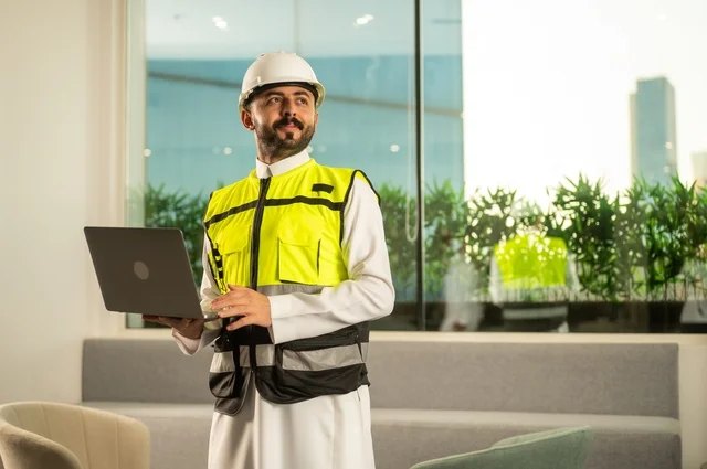 الاطلاع على تصاميم هندسية جديدة على جهاز الحاسوب المحمول، مهندس معماري عربي سعودي خليجي يرتدي اللباس الخاص بالعمل يستخدم اللابتوب، الاشراف الالكتروني على تطبيق المشاريع و الخطط الهندسيه المعمارية في البناء، دمج العمل مع التقنية و التكنولوجيا