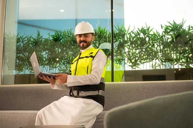 الاطلاع على تصاميم هندسية جديدة على جهاز الحاسوب المحمول، مهندس معماري عربي سعودي خليجي يرتدي اللباس الخاص بالعمل يستخدم اللابتوب، الاشراف الالكتروني على تطبيق المشاريع و الخطط الهندسيه المعمارية في البناء، دمج العمل مع التقنية و التكنولوجيا