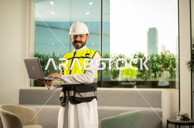 الاطلاع على تصاميم هندسية جديدة على جهاز الحاسوب المحمول، مهندس معماري عربي سعودي خليجي يرتدي اللباس الخاص بالعمل يستخدم اللابتوب، الاشراف الالكتروني على تطبيق المشاريع و الخطط الهندسيه المعمارية في البناء، دمج العمل مع التقنية و التكنولوجيا