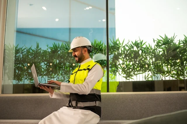 الاطلاع على تصاميم هندسية جديدة على جهاز الحاسوب المحمول، مهندس معماري عربي سعودي خليجي يرتدي اللباس الخاص بالعمل يستخدم اللابتوب، الاشراف الالكتروني على تطبيق المشاريع و الخطط الهندسيه المعمارية في البناء، دمج العمل مع التقنية و التكنولوجيا