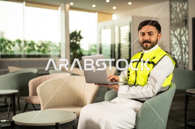 الاطلاع على تصاميم هندسية جديدة على جهاز الحاسوب المحمول، مهندس معماري عربي سعودي خليجي يرتدي اللباس الخاص بالعمل يستخدم اللابتوب، الاشراف الالكتروني على تطبيق المشاريع و الخطط الهندسيه المعمارية في البناء، دمج العمل مع التقنية و التكنولوجيا