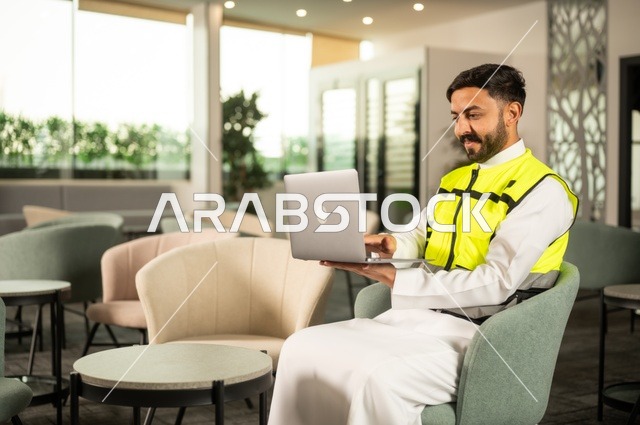 الاطلاع على تصاميم هندسية جديدة على جهاز الحاسوب المحمول، مهندس معماري عربي سعودي خليجي يرتدي اللباس الخاص بالعمل يستخدم اللابتوب، الاشراف الالكتروني على تطبيق المشاريع و الخطط الهندسيه المعمارية في البناء، دمج العمل مع التقنية و التكنولوجيا