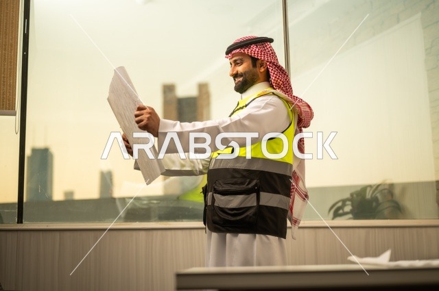 الإعمار بسواعد أبناء الوطن، مفهوم الهندسة والإنشاءات،  مهندس عربي خليجي سعودي يرتدي زي العمل يمسك بيده مخطط التطور العمراني للمباني، تدقيق ومراجعة الخطط الهندسية، دراسة أساسيات المشروع، إكمال رسم مخطوطات البناء