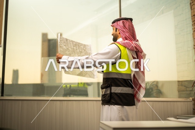 الإعمار بسواعد أبناء الوطن، مفهوم الهندسة والإنشاءات،  مهندس عربي خليجي سعودي يرتدي زي العمل يمسك بيده مخطط التطور العمراني للمباني، تدقيق ومراجعة الخطط الهندسية، دراسة أساسيات المشروع، إكمال رسم مخطوطات البناء