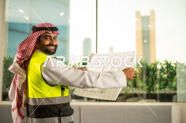 الإعمار بسواعد أبناء الوطن، مفهوم الهندسة والإنشاءات،  مهندس عربي خليجي سعودي يرتدي زي العمل يمسك بيده مخطط التطور العمراني للمباني، تدقيق ومراجعة الخطط الهندسية، دراسة أساسيات المشروع، إكمال رسم مخطوطات البناء