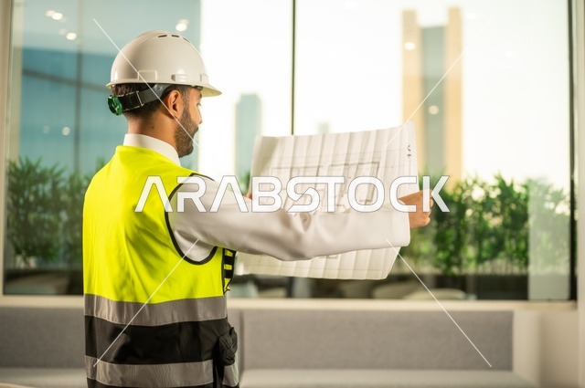 الإعمار بسواعد أبناء الوطن، مفهوم الهندسة والإنشاءات،  مهندس عربي خليجي سعودي يرتدي زي العمل يمسك بيده مخطط التطور العمراني للمباني، تدقيق ومراجعة الخطط الهندسية، دراسة أساسيات المشروع، إكمال رسم مخطوطات البناء