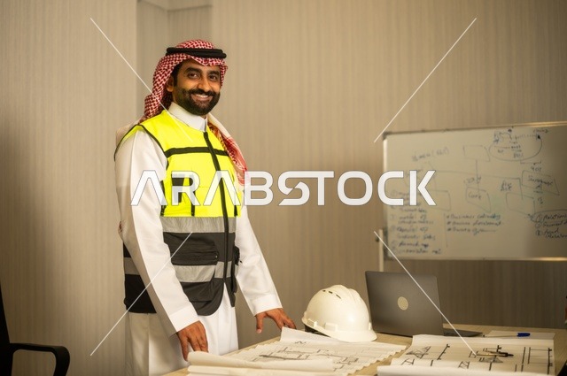 تدقيق ومراجعة الخطط الهندسية، دراسة أساسيات المشروع، إكمال رسم مخطوطات البناء، الإعمار بسواعد أبناء الوطن، مفهوم الهندسة والإنشاءات،  مهندس عربي خليجي سعودي يرتدي زي العمل يمسك بيده مخطط التطور العمراني للمباني