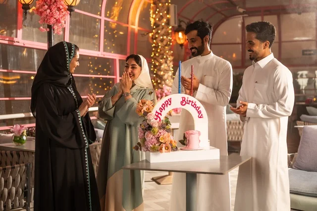 Spending quality time with family and friends, gestures of happiness, surprise, and joy, decorations for holidays and happy occasions, a family of Saudi Gulf Arabs celebrating their friend's birthday in a Saudi restaurant, a birthday cake.