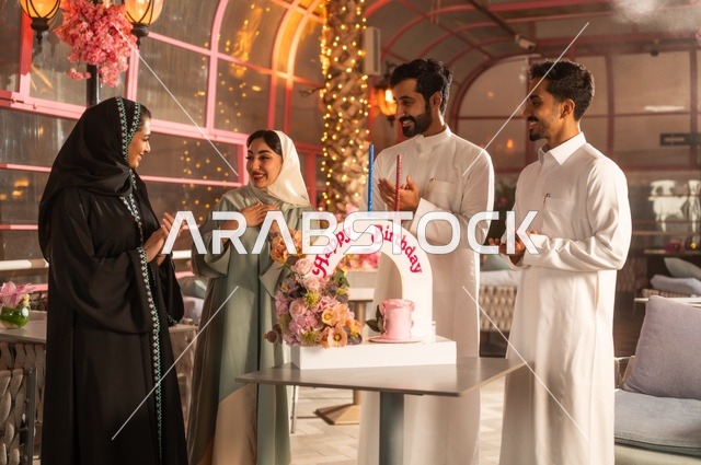 Spending quality time with family and friends, gestures of happiness, surprise, and joy, decorations for holidays and happy occasions, a family of Saudi Gulf Arabs celebrating their friend's birthday in a Saudi restaurant, a birthday cake.