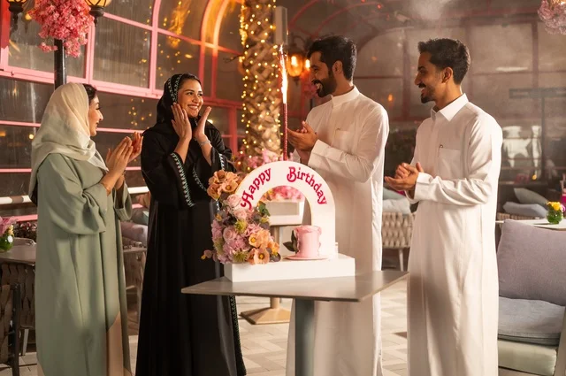 Spending quality time with family and friends, gestures of happiness, surprise, and joy, decorations for holidays and happy occasions, a family of Saudi Gulf Arabs celebrating their friend's birthday in a Saudi restaurant, a birthday cake.