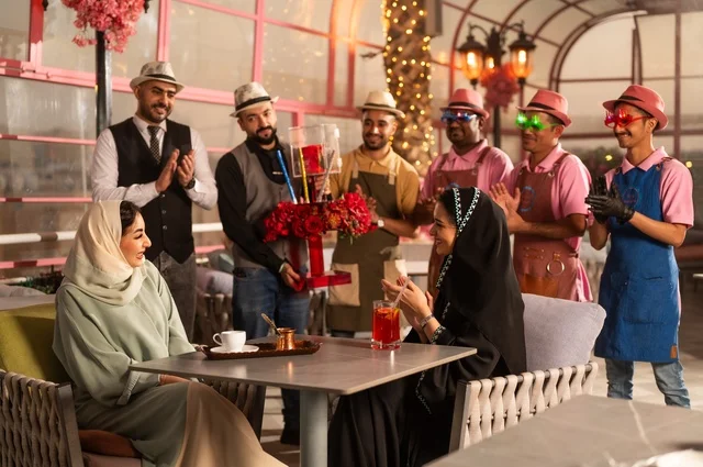 The service staff participates in the celebration, spending enjoyable time with friends, gestures of happiness and surprise, a Saudi Arabian Gulf woman wearing a hijab and an abaya celebrating her friend's birthday, decorating for happy occasions, holding birthday parties in cafes and luxury restaurants in the kingdom.