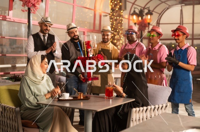 قامة حفلات اعياد الميلاد في الكافيهات والمطاعم الفاخرة في المملكة، التزيين  للاحتفال بالمناسبات السعيدة، إمشاركة طاقم الخدمة الاحتفال، قضاء وقت ممتع مع الأصدقاء، إيماءات السعادة والمفاجأة، امرأة عربية خليجية سعودية محجبة ترتدي العباءة تقوم بالاحتفال بعيد ميلاد صديقتها