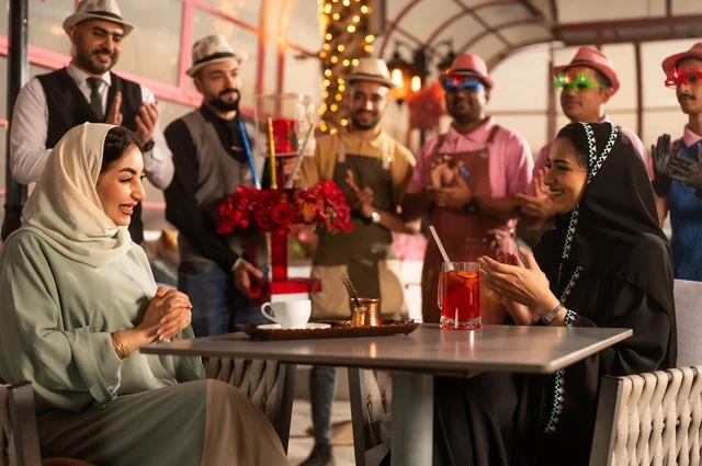 Birthday parties are held in cafes and luxury restaurants in the kingdom, with decorations to celebrate happy occasions, sharing the celebration with the service staff, spending enjoyable time with friends, gestures of happiness and surprise, an Arab Gulf Saudi woman wearing a hijab and an abaya is celebrating her friend's birthday.