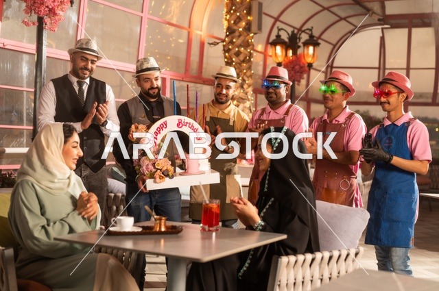 التزيين  للاحتفال بالمناسبات السعيدة، إقامة حفلات اعياد الميلاد في الكافيهات والمطاعم الفاخرة في المملكة، مشاركة طاقم الخدمة الاحتفال، قضاء وقت ممتع مع الأصدقاء، إيماءات السعادة والمفاجأة، امرأة عربية خليجية سعودية محجبة ترتدي العباءة تقوم بالاحتفال بعيد ميلاد صديقتها