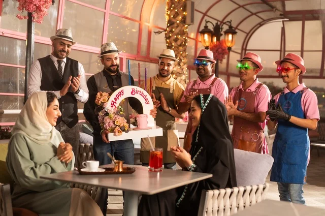Decoration for celebrating happy occasions, holding birthday parties in cafes and luxury restaurants in the kingdom, sharing the celebration with the service staff, having a good time with friends, gestures of happiness and surprise, an Arab Gulf Saudi woman wearing a hijab and an abaya celebrating her friend's birthday.