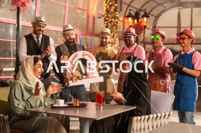 قامة حفلات اعياد الميلاد في الكافيهات والمطاعم الفاخرة في المملكة، التزيين  للاحتفال بالمناسبات السعيدة، إمشاركة طاقم الخدمة الاحتفال، قضاء وقت ممتع مع الأصدقاء، إيماءات السعادة والمفاجأة، امرأة عربية خليجية سعودية محجبة ترتدي العباءة تقوم بالاحتفال بعيد ميلاد صديقتها