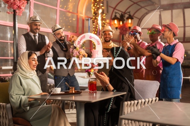 قامة حفلات اعياد الميلاد في الكافيهات والمطاعم الفاخرة في المملكة، التزيين  للاحتفال بالمناسبات السعيدة، إمشاركة طاقم الخدمة الاحتفال، قضاء وقت ممتع مع الأصدقاء، إيماءات السعادة والمفاجأة، امرأة عربية خليجية سعودية محجبة ترتدي العباءة تقوم بالاحتفال بعيد ميلاد صديقتها