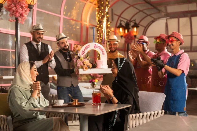 The service staff participates in the celebration, spending enjoyable time with friends, gestures of happiness and surprise, a Saudi Arabian Gulf woman wearing a hijab and an abaya celebrating her friend's birthday, decorating for happy occasions, holding birthday parties in cafes and luxury restaurants in the kingdom.